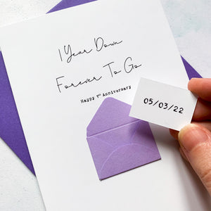 A Wedding Anniversary Date on a token, being hidden inside a mini handmade envelope on the front of a 1st Anniversary Greeting Card. The card reads 1 Year Down Forever To Go, Happy 1st Anniversary.