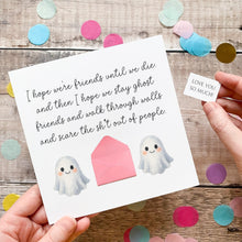 Load image into Gallery viewer, a person holding a card with a message and two ghostly figures, surrounded by colorful confetti on a wooden surface.